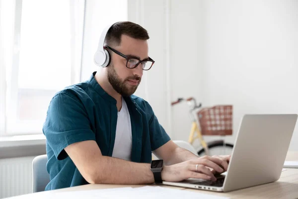 Male employee in wireless headphones work on laptop — Stock Photo, Image