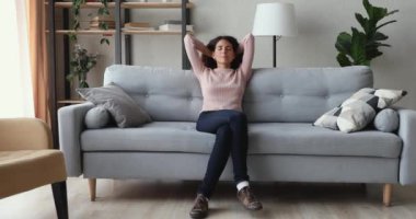 Huzurlu, gülümseyen bir kadın, kanepede uzanmış kafasının arkasında rüya görüyor.