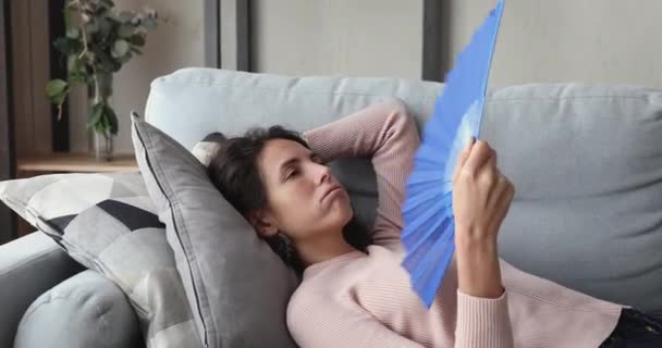 Mujer joven sobrecalentada o enferma agitando ventilador acostado en el sofá — Vídeos de Stock