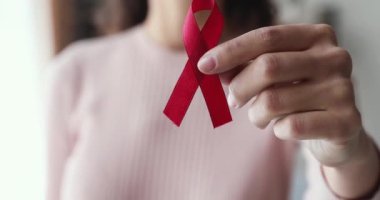 Elinde kırmızı kurdele tutan genç bir kadın kameraya gösteriyor.