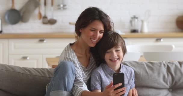 Madre feliz y el hijo de la escuela riendo usando el teléfono inteligente en casa — Vídeo de stock