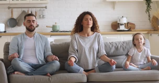 Gezond ouders en kind dochter mediteren samen zitten op de bank — Stockvideo