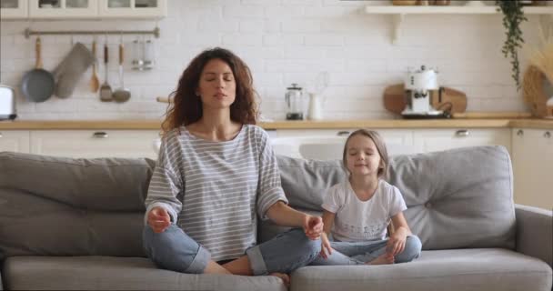 Запоминающаяся мама учит маленького ребенка дочь медитировать вместе на диване — стоковое видео