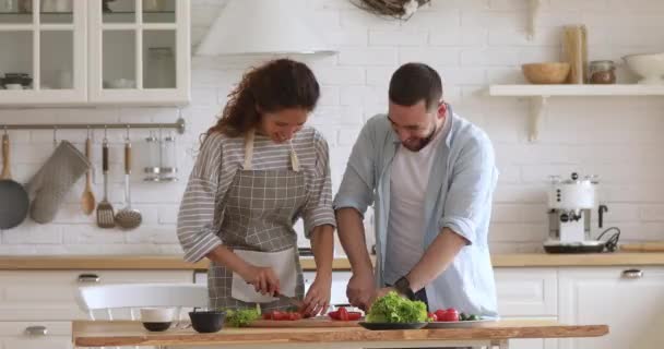 Glimlachend jong paar snijden salade praten samen koken in keuken — Stockvideo