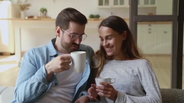 Счастливые любящие супруги отдыхают на диване, пьют горячий чай . — стоковое видео