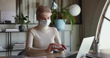 Maske takan kadın ofis çalışanı dezenfektan jöle ile ellerini temizliyor.