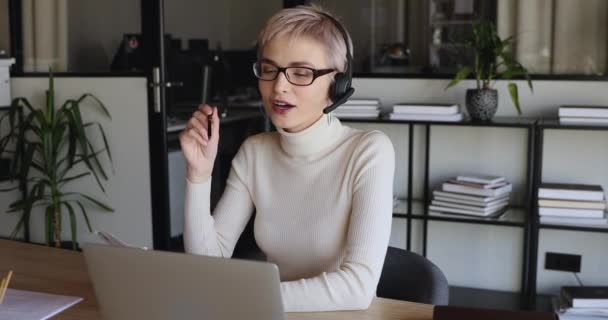 Trabajadora de oficina sonriente con auriculares comunicándose por videollamada — Vídeos de Stock