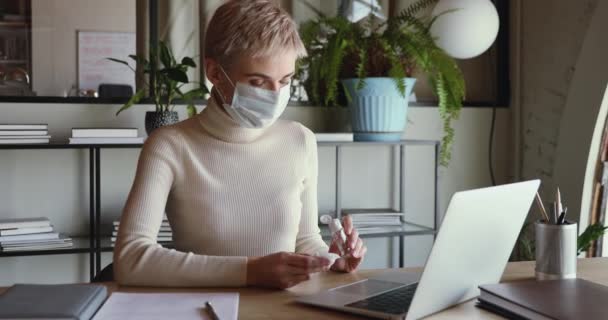 Geschäftsfrau trägt medizinische Gesichtsmaske und reinigt Laptop-Tastatur mit Desinfektionsmittel — Stockvideo