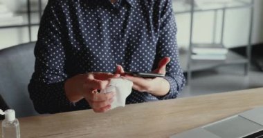 Hintli iş kadını sağlık maskesi takıyor. Cep telefonunu dezenfektanla temizliyor.