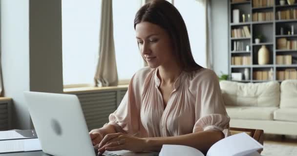 Focused young woman sitting at table, typing message on computer. — Stock Video