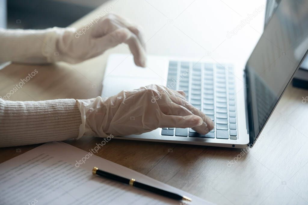 Young cautious businesswoman working on computer in gloves.