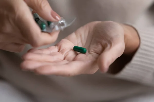 Middle aged woman pouring capsules pills out of plastic blister.