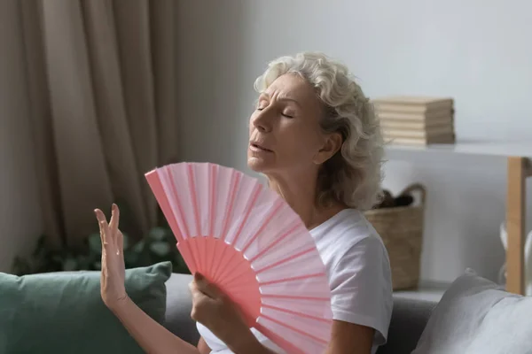 Stressed middle aged retired woman using paper fan.