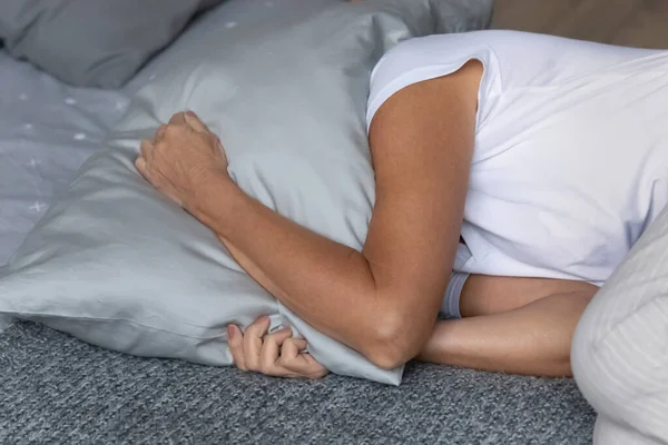 Stressed older mature retired woman covering head with pillow.