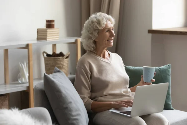 Senior kvinna sitter på soffan, njuter av morgontid. — Stockfoto