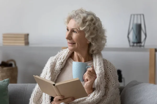 Seniorin hält Papierbuch und heißen Tee in der Hand. — Stockfoto