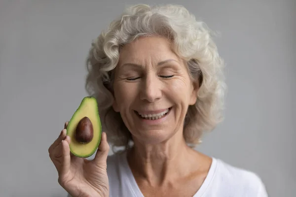 Feliz meia idade aposentado senhora segurando fatia de abacate maduro . — Fotografia de Stock