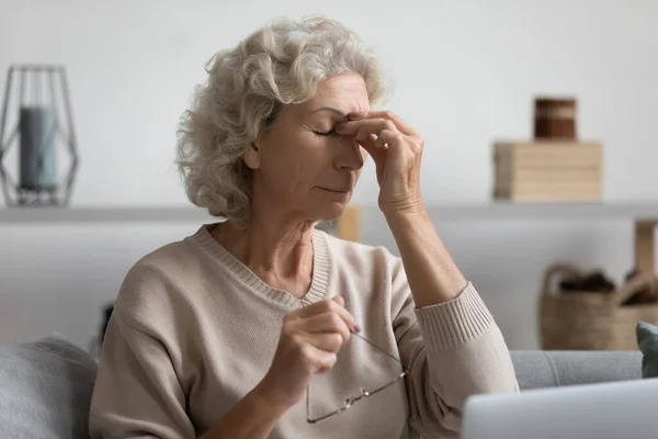 Middle aged grandmother rubbing eye, feeling tired.