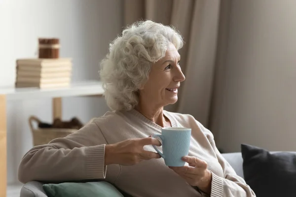 Calm mature woman dreaming of future with cup of tea.