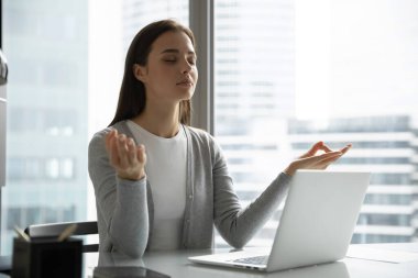 Genç kadın çalışan, işyerinde yoga yaparken meditasyon yapıyor.