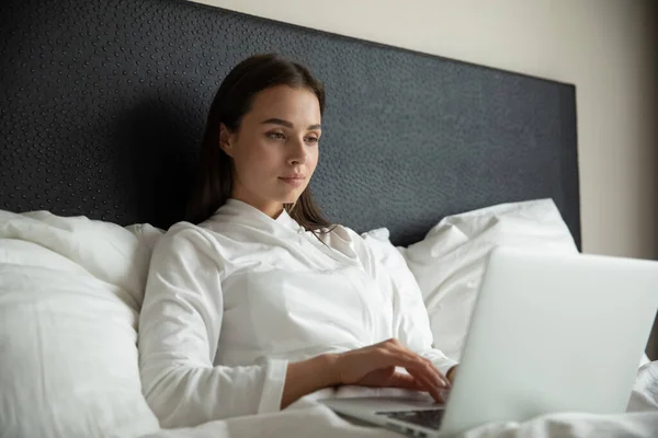 Giovane donna d'affari impegnata a lavorare sul computer portatile a letto — Foto Stock
