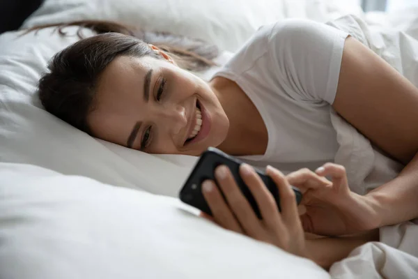 Mosolygó fiatal nő pihentető az ágyban segítségével sejt — Stock Fotó