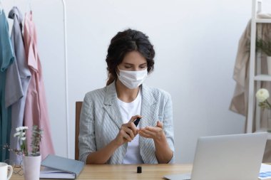 Koruyucu tıbbi maskeli genç bir kadın ellerini antiseptikle temizliyor..