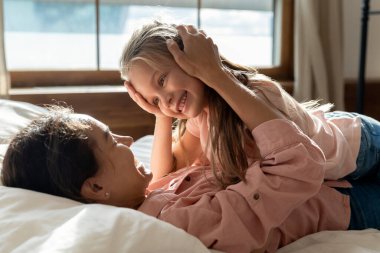 Mutlu anne yatakta yatıyor, küçük kızın kafasını okşuyor..