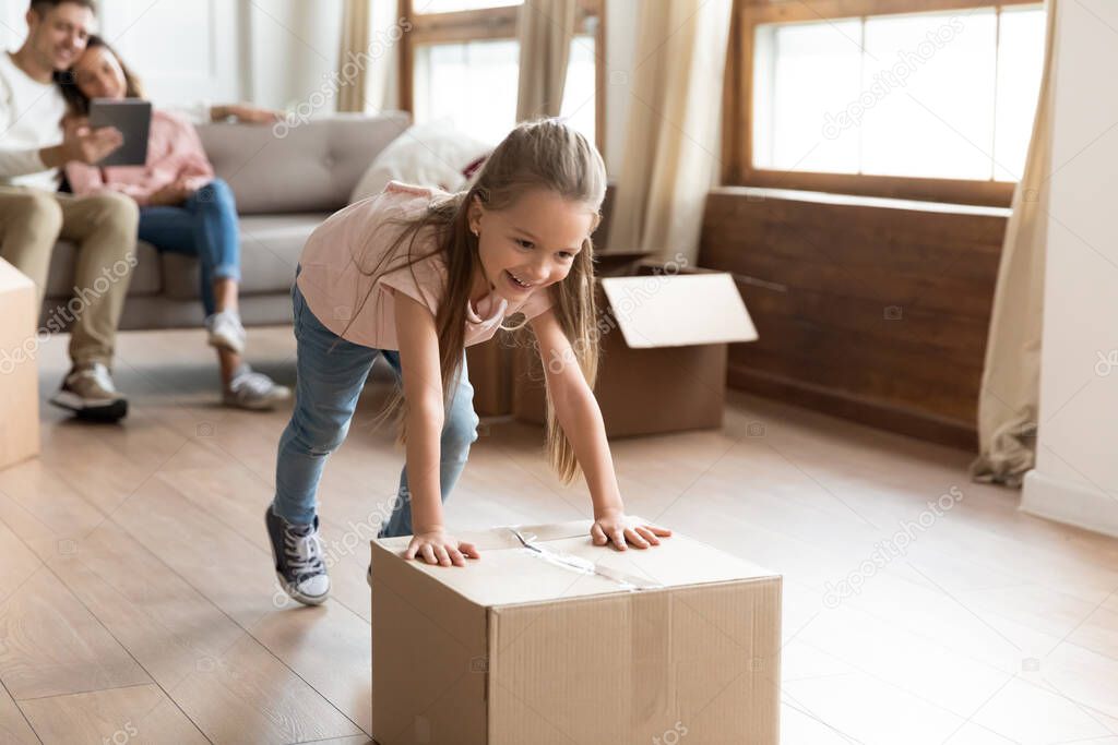 Overjoyed little girl running pushing cardboard boxes in new house.