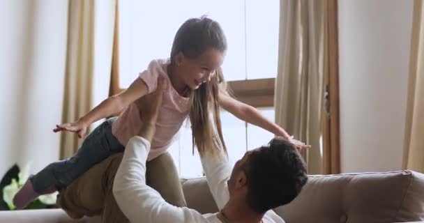 Joven padre acostado en el sofá, levantando la hija del niño riendo . — Vídeos de Stock