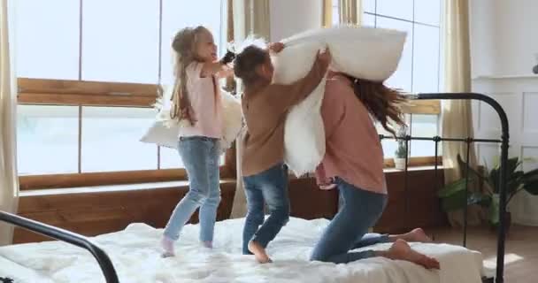 Kleine entzückende Schwestern Kinder kämpfen mit lächelnder Mutter gegen Kissen. — Stockvideo