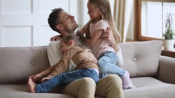 Щасливий батько розслабляється на дивані з милими маленькими дівчатками . — стокове відео