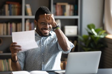 Happy mixed race businessman celebrating triumph, reading letter with news.