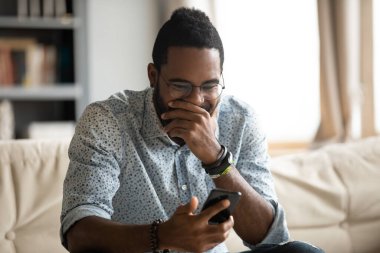 Funny young african ethnicity guy looking at cellphone screen.