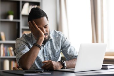 Tired young african man leaning on hand, sleeping at table.