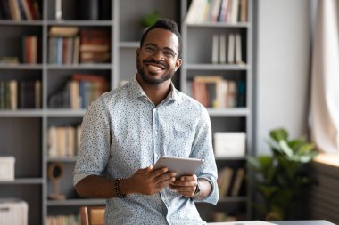 Smiling young biracial man in glasses holding digital computer tablet.