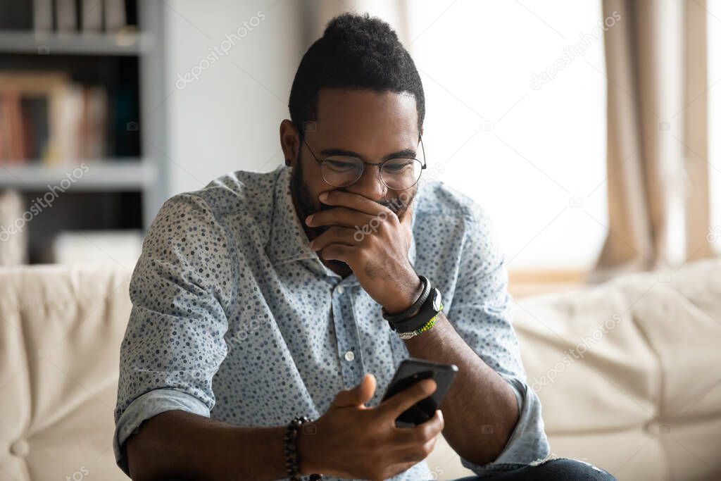 Funny young african ethnicity guy looking at cellphone screen.
