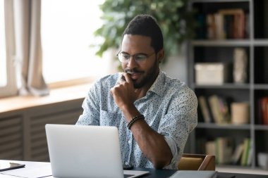 Smiling handsome young african american guy looking at computer screen.