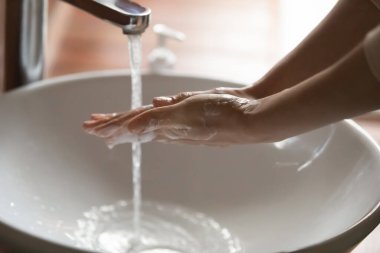 Banyo lavabosunun üstünde ellerini yıkayan genç bir kadın.