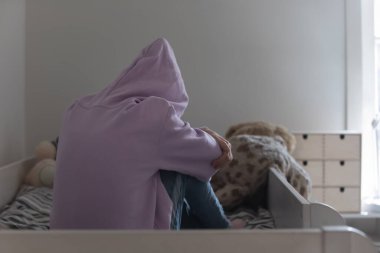 Kapüşonlu yalnız genç kız yatakta tek başına ağlıyor.