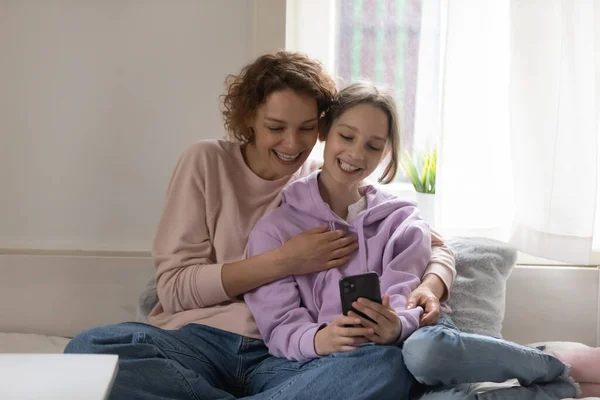 Happy teen daughter and young mum using smartphone at home