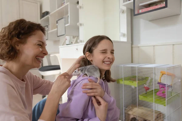 Cheerful mom and teenage daughter laughing playing with rat pet