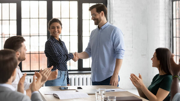 Smiling businessman handshake indian female employee at team meeting