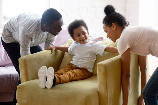 Glückliches afrikanisch-amerikanisches Paar bewegt Sessel mit kleinem Sohn. — Stockfoto