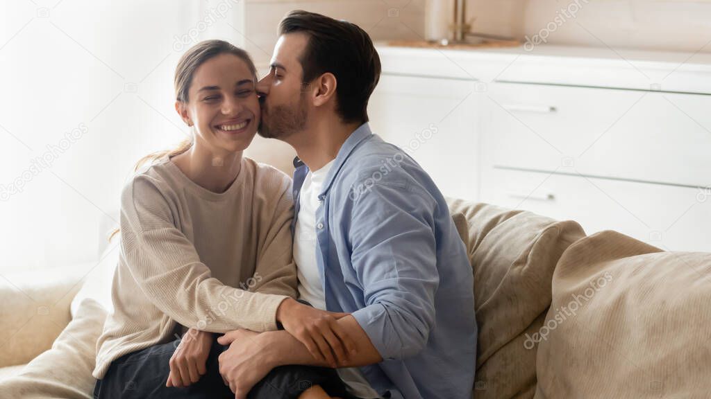 Affectionate young bearded man kissing cheek of beloved smiling girlfriend.