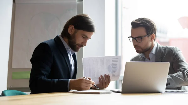 Vážné mužské kolegové pracují na notebooku v kanceláři společně — Stock fotografie