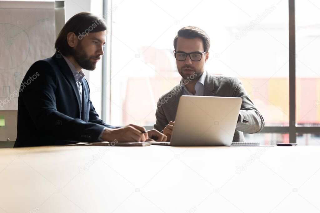 Male coworkers sit at meeting working on laptop together