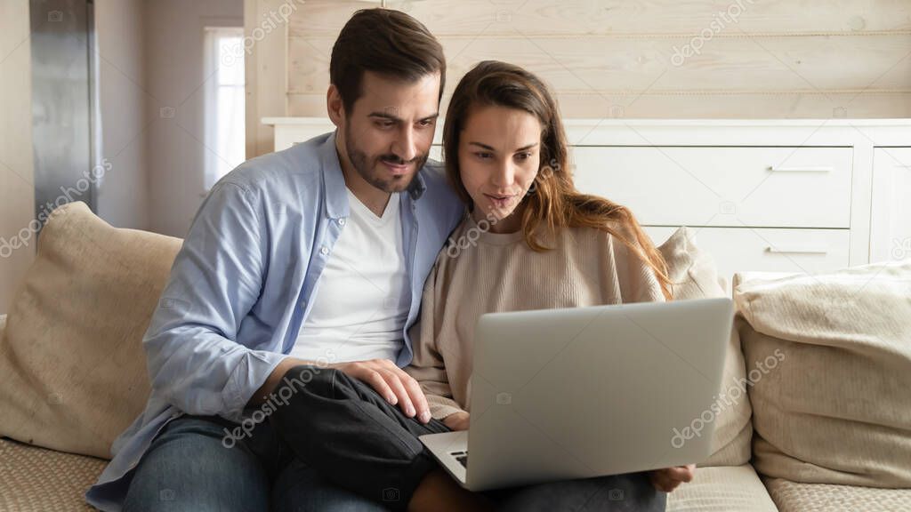 Happy millennial married couple looking at computer monitor at home.