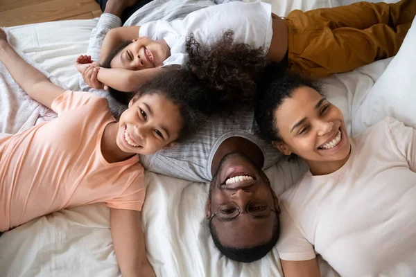 Pais americanos africanos felizes com crianças pequenas deitadas na cama . — Fotografia de Stock