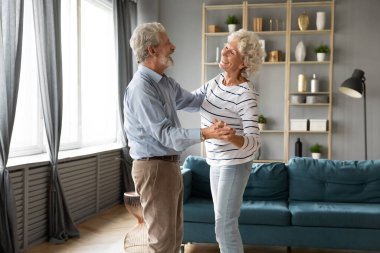 Mutlu yaşlı adam ve kadın rahat oturma odasında dans ediyor.